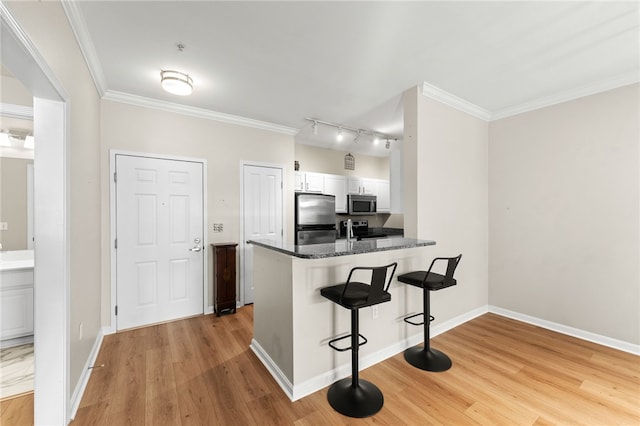 kitchen featuring crown molding, appliances with stainless steel finishes, light wood-style floors, white cabinetry, and a kitchen breakfast bar