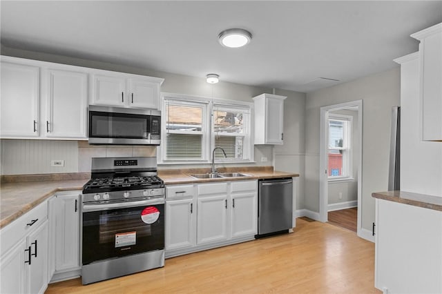 kitchen with light wood finished floors, appliances with stainless steel finishes, white cabinetry, a sink, and baseboards