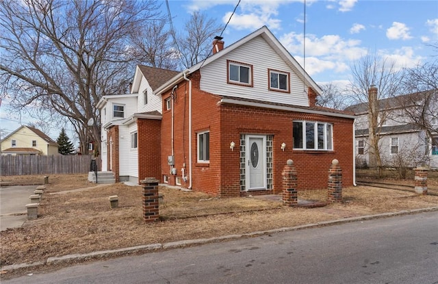 view of front of house with a shingled roof, a chimney, fence, and brick siding