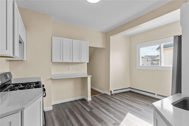 kitchen featuring stainless steel gas range oven, baseboards, dark wood-type flooring, light stone countertops, and white cabinetry