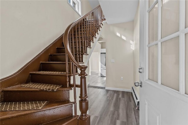 foyer entrance with a towering ceiling, a baseboard radiator, baseboards, and wood finished floors