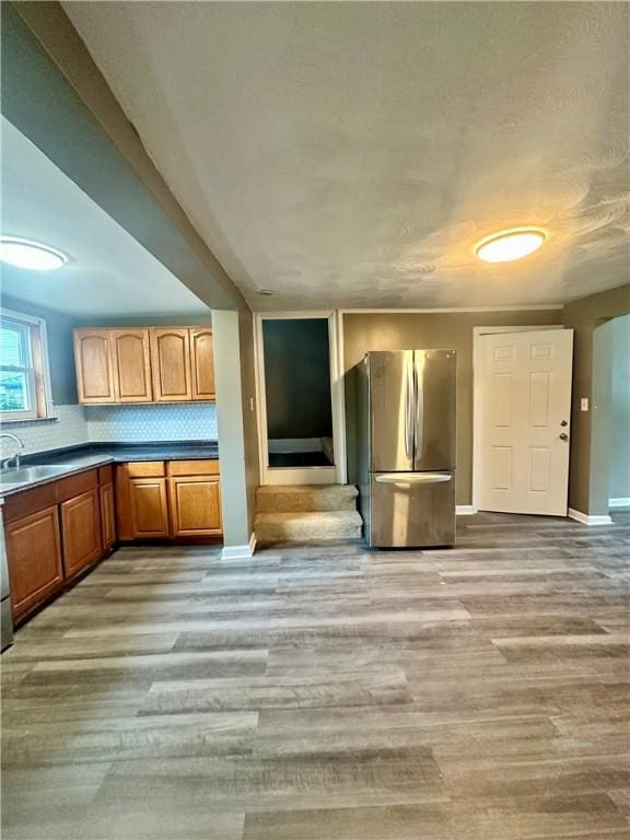 kitchen with a sink, baseboards, light wood-style floors, freestanding refrigerator, and tasteful backsplash