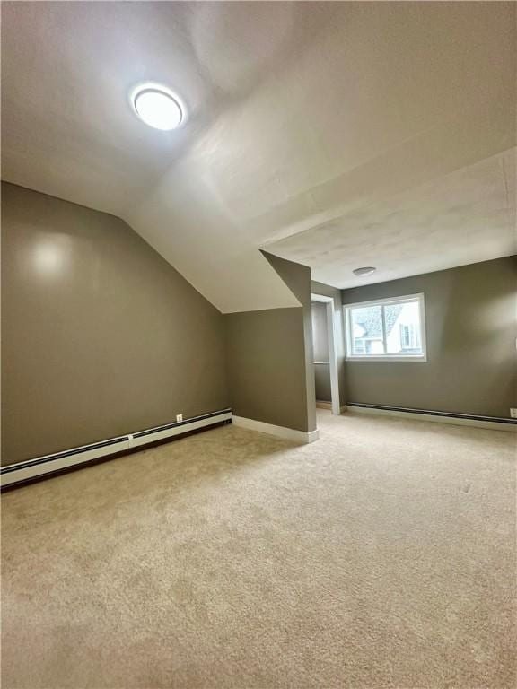 additional living space with a baseboard heating unit, light colored carpet, vaulted ceiling, and baseboards