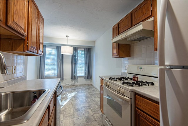 kitchen with white appliances, baseboards, brown cabinets, under cabinet range hood, and backsplash