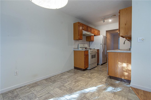 kitchen featuring white appliances, brown cabinets, light countertops, under cabinet range hood, and a sink