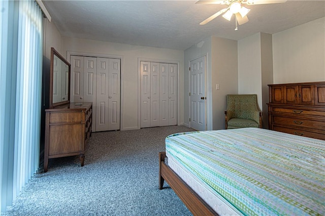 bedroom featuring light carpet, baseboards, ceiling fan, a textured ceiling, and two closets