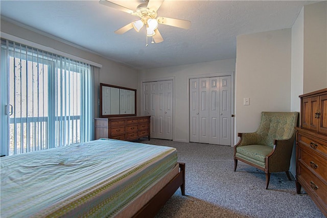 bedroom with a textured ceiling, carpet, two closets, and a ceiling fan