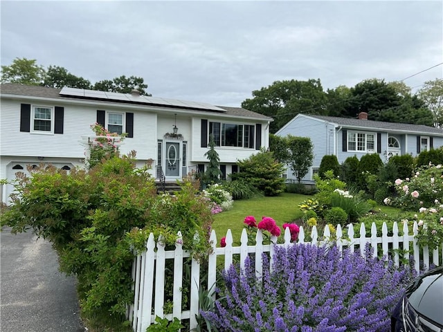 view of front facade featuring a front lawn, a fenced front yard, and roof mounted solar panels