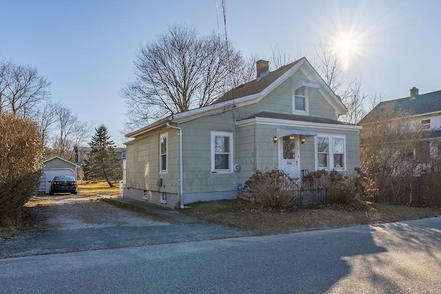 bungalow-style home with a chimney, aphalt driveway, and an outbuilding