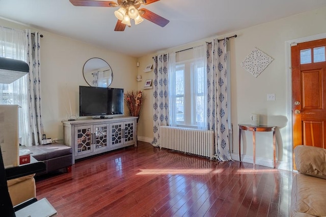 living area featuring a wealth of natural light, baseboards, radiator heating unit, and wood finished floors