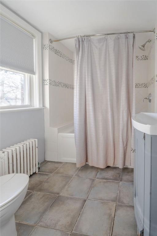 bathroom featuring shower / bath combination with curtain, radiator, a sink, and toilet