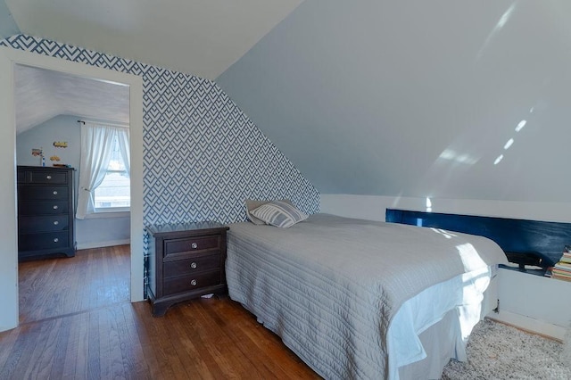 bedroom with an accent wall, baseboards, vaulted ceiling, hardwood / wood-style floors, and wallpapered walls