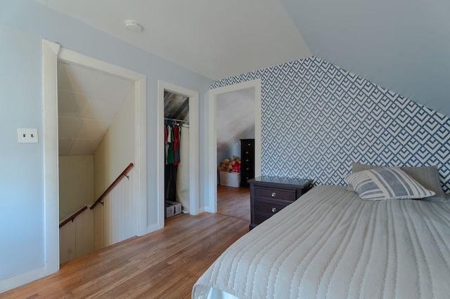 bedroom with an accent wall, baseboards, vaulted ceiling, a closet, and light wood-type flooring