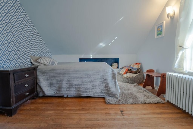 bedroom with radiator, wood finished floors, and lofted ceiling