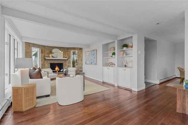 living area with beamed ceiling, built in features, baseboard heating, a stone fireplace, and wood-type flooring