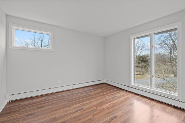 unfurnished room with a healthy amount of sunlight, a baseboard heating unit, and wood finished floors