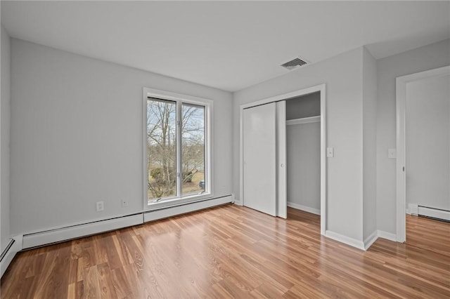 unfurnished bedroom with wood finished floors, visible vents, baseboards, a closet, and a baseboard heating unit