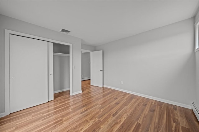 unfurnished bedroom with a baseboard radiator, light wood-style floors, baseboard heating, and a closet