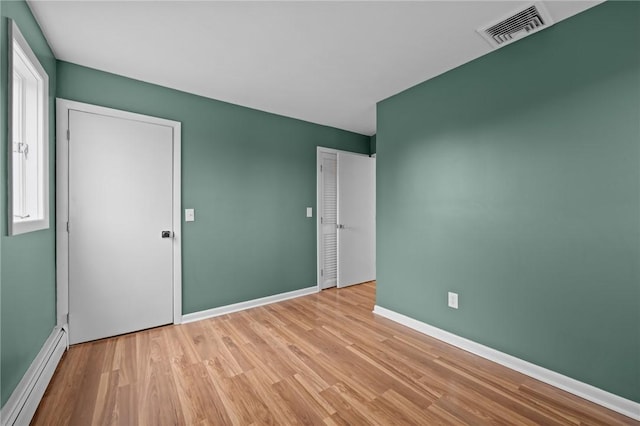 spare room with visible vents, baseboard heating, baseboards, and wood finished floors