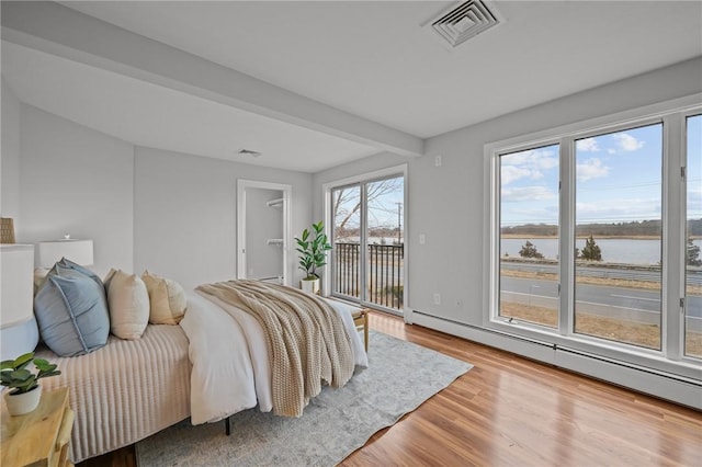 bedroom with visible vents, a water view, access to outside, wood finished floors, and a baseboard radiator