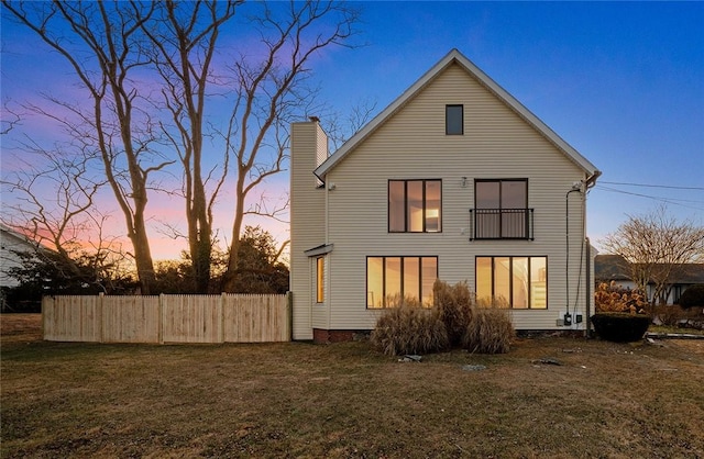 back of property at dusk featuring a yard, fence, and a chimney