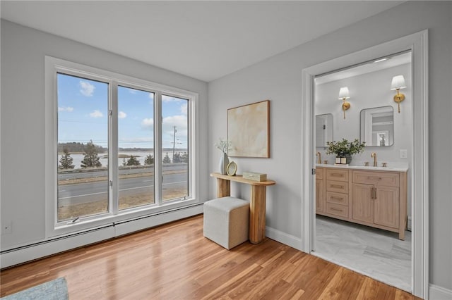 living area with a wealth of natural light, baseboard heating, light wood-type flooring, and baseboards