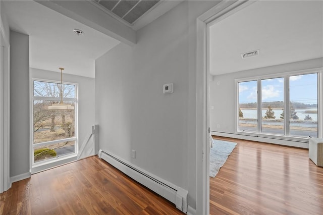 empty room with a baseboard heating unit, visible vents, and wood finished floors