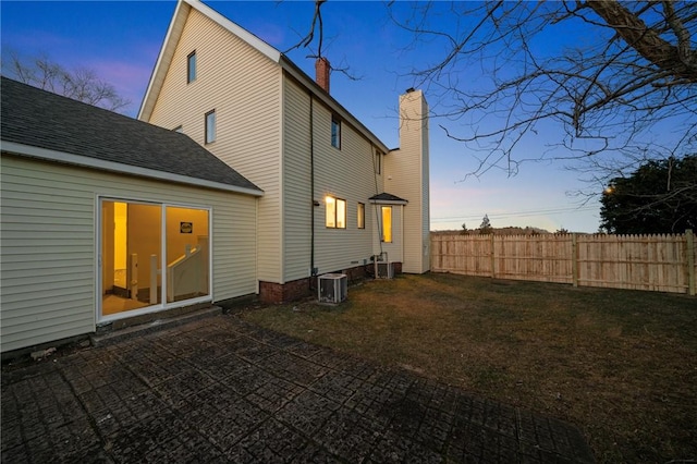 back of house at dusk featuring a yard, a patio area, cooling unit, and fence