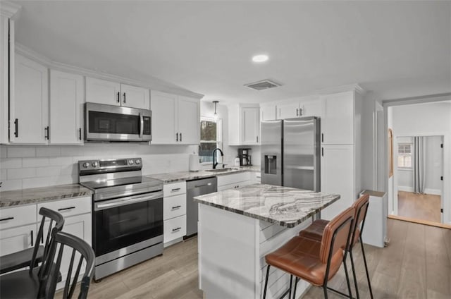 kitchen featuring a breakfast bar area, stainless steel appliances, visible vents, white cabinetry, and a sink