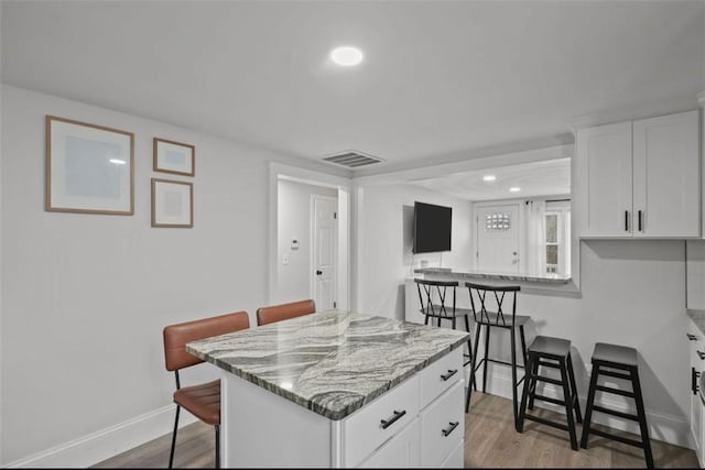 kitchen featuring a breakfast bar, wood finished floors, white cabinetry, baseboards, and light stone countertops