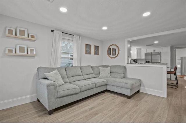 living area with baseboards, light wood finished floors, and recessed lighting