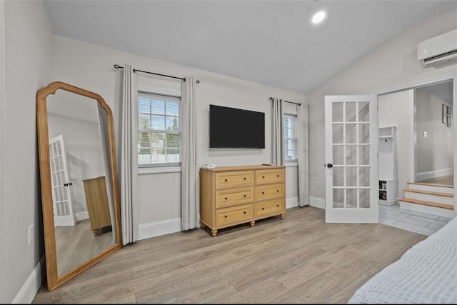 bedroom with light wood finished floors, baseboards, a wall unit AC, lofted ceiling, and french doors