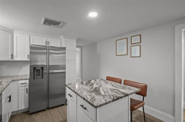 kitchen with stainless steel fridge, a kitchen island, visible vents, and wood finished floors