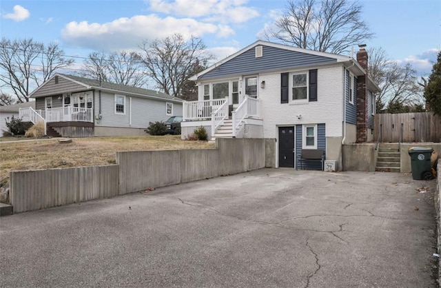 view of front of home with driveway, a chimney, fence, a porch, and brick siding