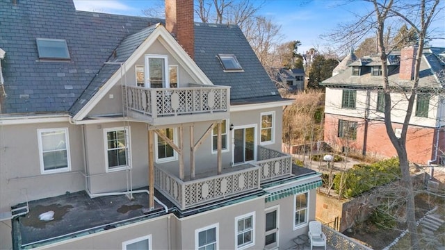 back of property featuring a balcony, a chimney, and stucco siding