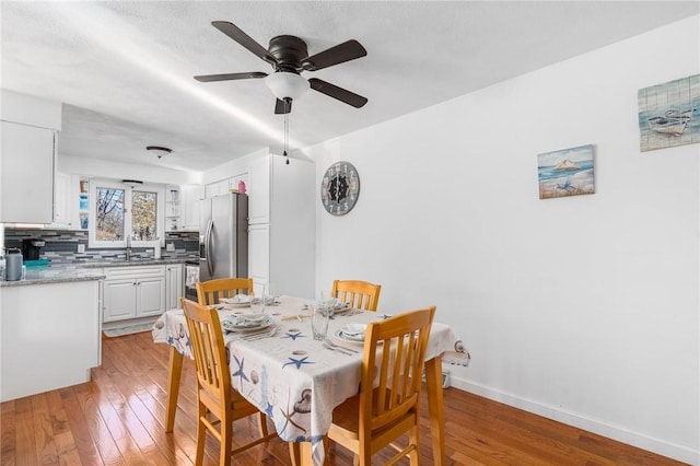 dining room with light wood finished floors, a ceiling fan, and baseboards