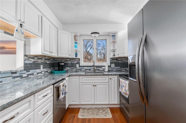 kitchen featuring stainless steel appliances, a sink, white cabinetry, light wood-type flooring, and tasteful backsplash