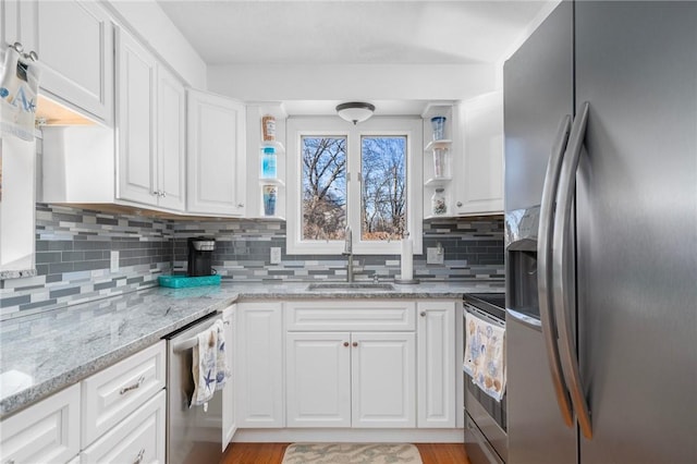 kitchen with light stone counters, decorative backsplash, appliances with stainless steel finishes, white cabinetry, and a sink