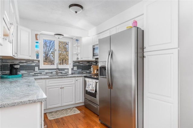 kitchen with white cabinets, decorative backsplash, light wood-style flooring, stainless steel appliances, and a sink