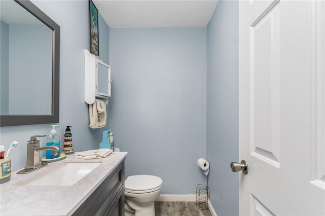 bathroom with toilet, baseboards, wood finished floors, and vanity