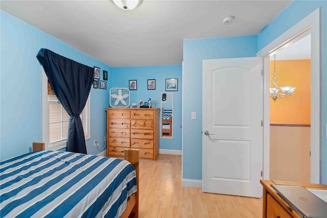 bedroom featuring baseboards, light wood-type flooring, and a notable chandelier