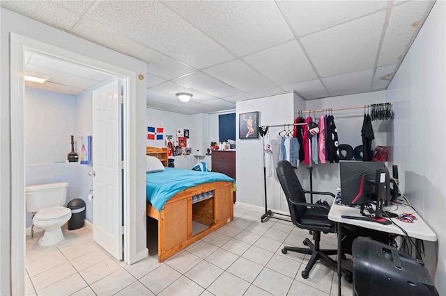 bedroom with a drop ceiling, ensuite bath, and light tile patterned floors