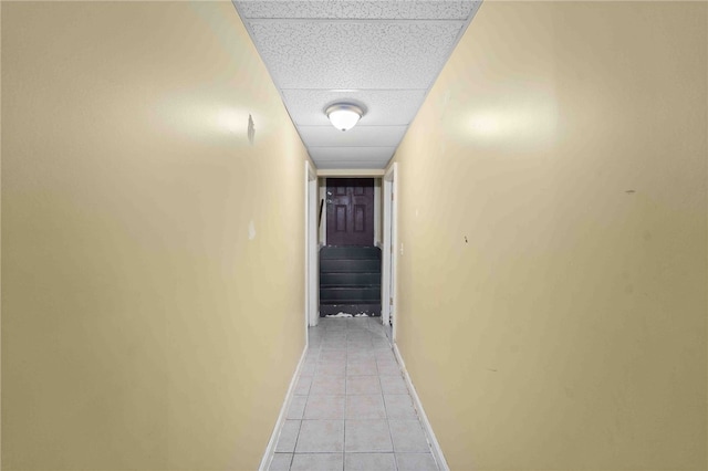 hallway featuring a paneled ceiling, light tile patterned flooring, baseboards, and stairs