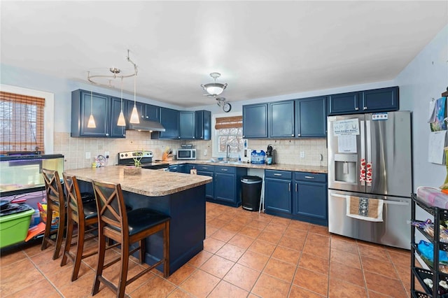 kitchen featuring tasteful backsplash, appliances with stainless steel finishes, a sink, blue cabinets, and a peninsula