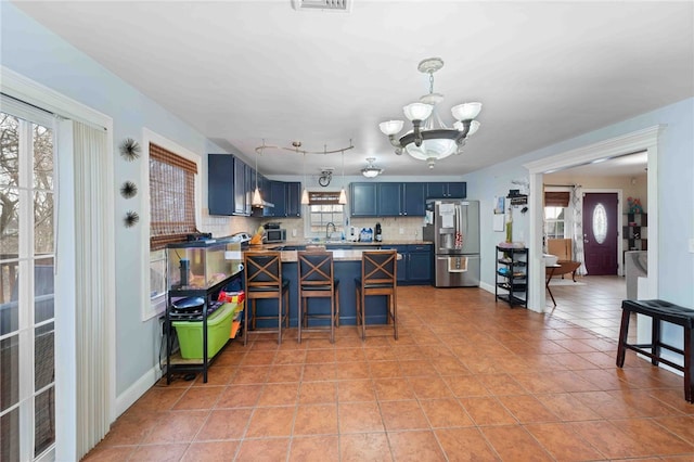 kitchen featuring a peninsula, a healthy amount of sunlight, stainless steel fridge with ice dispenser, blue cabinetry, and decorative backsplash