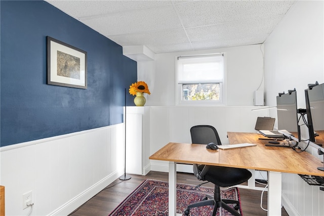 office space with a drop ceiling, a wainscoted wall, and wood finished floors