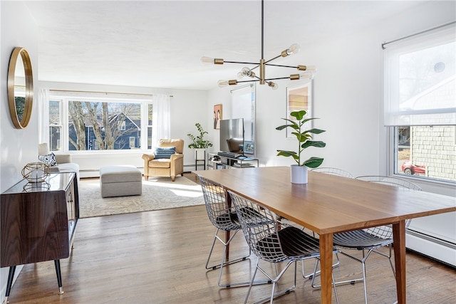 dining space with a baseboard radiator, an inviting chandelier, and wood finished floors