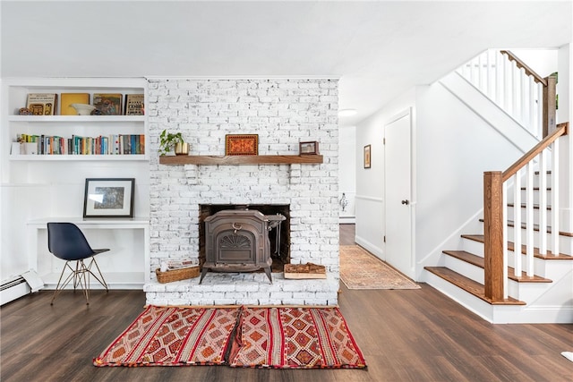 living room featuring wood finished floors, stairway, a baseboard radiator, baseboards, and a wood stove