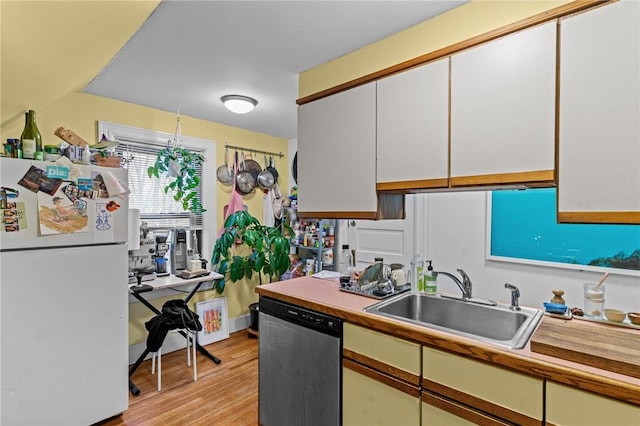 kitchen featuring freestanding refrigerator, a sink, light countertops, light wood-type flooring, and stainless steel dishwasher