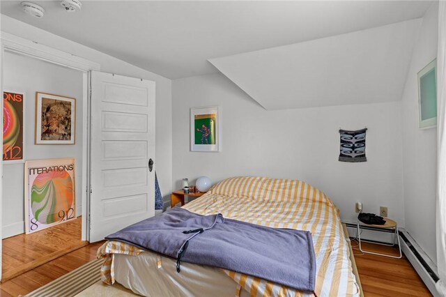 bedroom with baseboard heating, a baseboard heating unit, vaulted ceiling, and wood finished floors